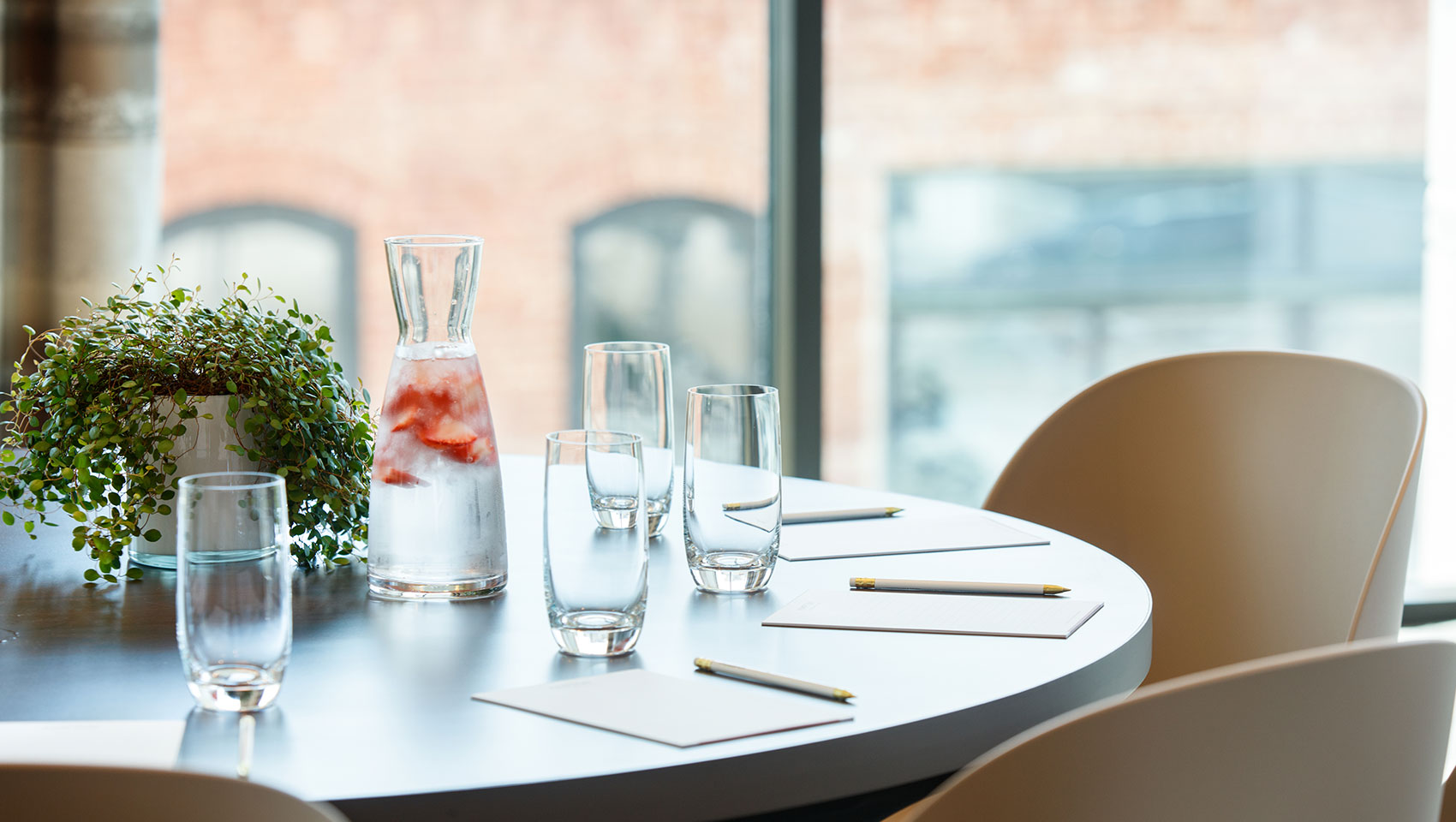 close up of meeting table with glasses, water, paper, pens and a plant